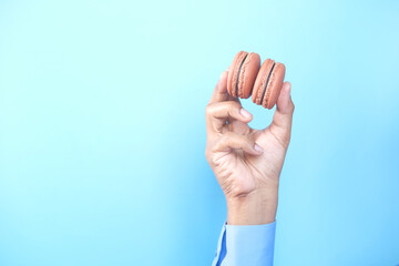 Fototapeta premium hand holding chocolate macaroon against blue background 