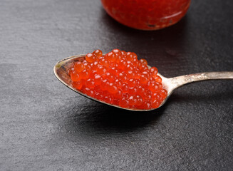 red caviar of chum salmon in a metal spoon on a black background