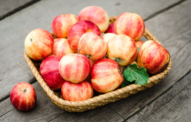 red garden apples lie in  small wicker basket on an old wooden background.