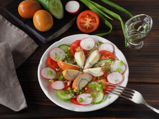 Slices of smoked egg, tomatoes, cucumber, radish with green onions and spices in a plate, fork, olive oil on a dark wooden table, flat layout. Recipe for vitamin salad with chicken eggs