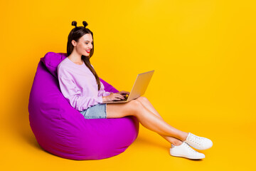 Full size photo of young smiling positive good mood girl sit armchair working in laptop isolated on yellow color background