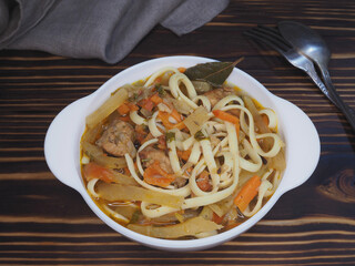 Asian hot lagman soup with noodles, meat, vegetables, national spices in a white bowl on with napkin, spoon, fork a wooden table, top view, flat layout. Delicious dish laghman 