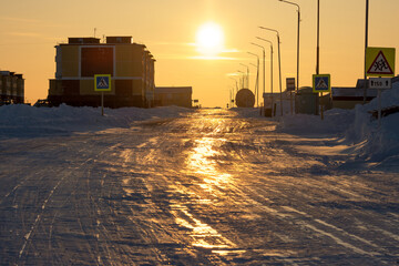 View of the street and buildings of a small arctic village at sunset. Bright golden sunlight. Winter arctic landscape. Daily life in the far north. Cold weather. Tavayvaam, Chukotka, Siberia, Russia.
