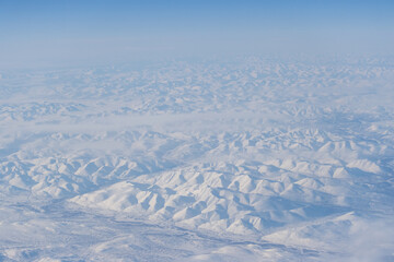 Aerial view of snow-capped mountains and clouds. Winter snowy mountain landscape. Travel to the far north of Russia. Kolyma Mountains, Magadan Region, Siberia, Russian Far East. Beautiful background.