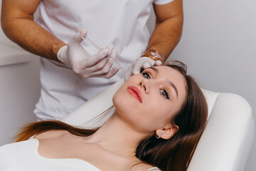 Obraz na płótnie Canvas Young brunette woman receiving plastic surgery injection on her face, closeup portrait