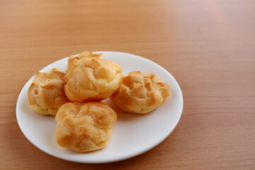 Round shape choux cream group on round white dish  and light brown wood background.