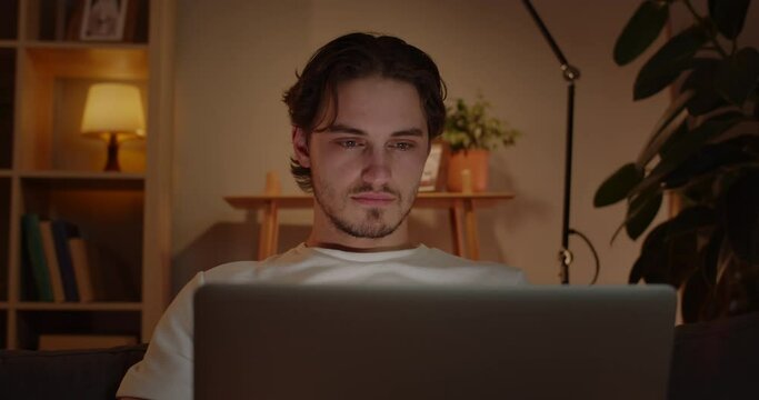 Crop view of handsome man using laptop while sitting on sofa at home. Caucasian guy browsing internet and looking at computer screen.Concept of free time and leisure.