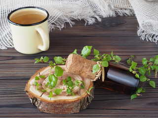 Twigs with green leaves and birch buds, drinking birch juice extract in a bottle, herbal tea in a mug on a dark wooden background, closeup. Useful betula plant for use in medicine, homeopathy 