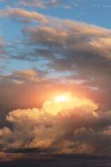 Epic sunset storm sky with sun and yellow orange sunlight. Big dark fluffy cumulus clouds on blue sky background texture