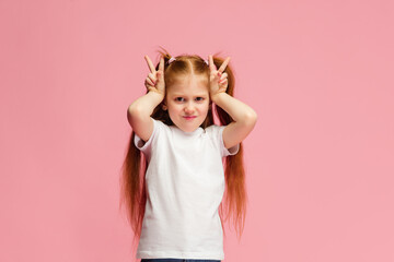 Funny gremacing. Happy, smiley little caucasian girl isolated on pink studio background with copyspace for ad. Looks happy, cheerful. Childhood, education, human emotions, facial expression concept.