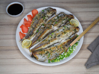 Fried fish micromesistius poutassou with lemon, pickled ginger in a plate, soy sauce and chopsticks on the table, flat layout. Healthy seafood for dietary nutrition, delicious light snack for beer