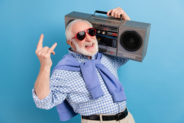 Photo of optimistic old grey hairdo man show rock sign hold boom-box wear spectacles blue shirt isolated on color background