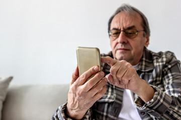 Elderly man using a mobile phone while relaxing at home. Smiling senior man wearing eyeglasses peer down at his smart phone as he tap out a text. Technology, people and lifestyle concept. Copy space.