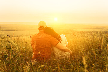 A couple in love is hugging and sitting close against the backdrop of bright orange sunset on the hill. Romantic summertime. Unrecognizable people
