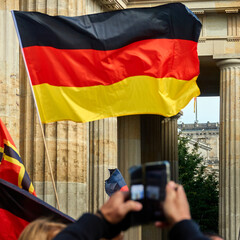 Black red golden flag of Germany waving at the Anticorona demonstration in front of the Brandenburg...