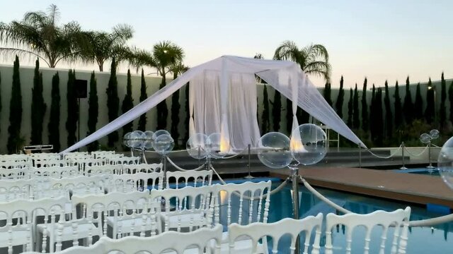 Jewish traditions wedding outdoor ceremony. Wedding canopy (chuppah, hupa) made of white fabric against the background of evening sky, palms and an artificial reservoir decorated with balloons. HD