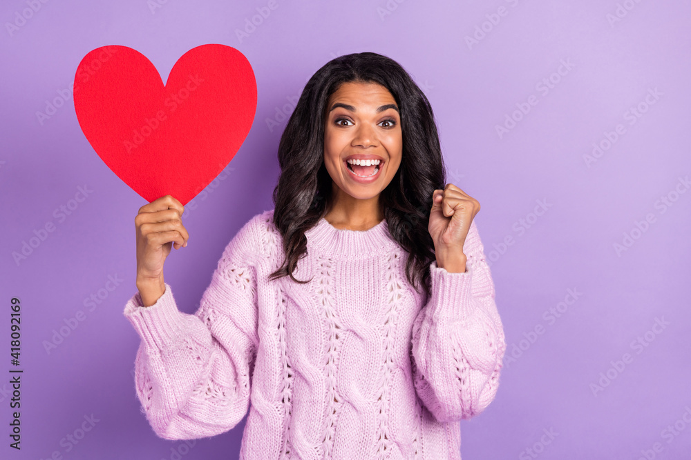 Wall mural Photo of young girl happy smile rejoice victory success hold big red paper heart fists hand isolated over purple color background