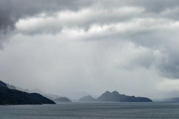 Mesmerizing view of the sea surrounded with mountains under the cloudy and rainy sky