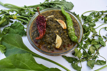 Indian homemade curry Sarson ka saag ki sabji served in transparent bowl garnished with fried green chilly, red chilly and garlic cloves. Authentic North indian Punjabi sabzi. Decorated with raw leaf
