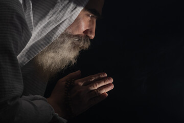 A senior man standing in dark smoky background light ray from above. Prayer gesture.
