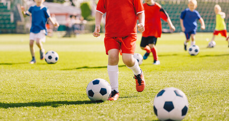 Sporty children on football summer camp. Kids practicing football on grass field. Football soccer children training class. Group of school children running and kicking soccer balls on training camp