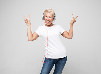 happy senior woman with short white hair wearing white tshirt listening to music with headphones