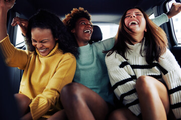 Diverse young female friends laughing in the backseat of a car