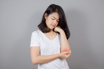 Portrait of Asian teenager wears white t-shirt having pain in injured elbow on gray background, Health care and arm pain concept