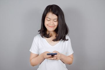 Portrait of smiling Asian teenager wears white t-shirt she is using mobile phone or smartphone isolated on gray background