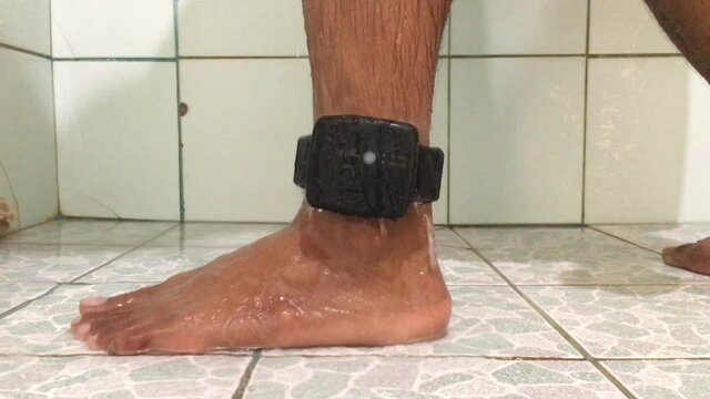 A male prisoner taking a shower In the bathroom there are white tiles. With a Electronic Monitoring (EM) to the leg Waterproof, no short circuit.