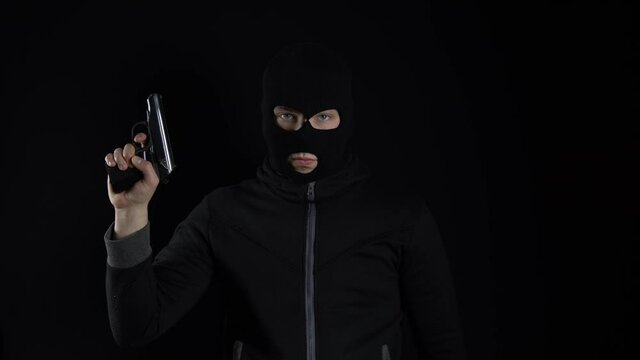 A man in a balaclava mask stands with a gun. The b