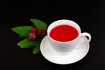 Roselle tea or Hibiscus sabdariffa juice in white ceramic cup and fresh roselle black wooden background. Drink herbal water for health care.