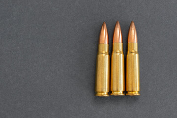 Three bullets on gray paper background. Cartridges 7.62 caliber for Kalashnikov assault rifle, closeup with copy space