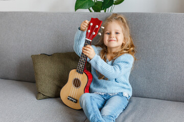Cute little girl playing ukulele and tuning it at home. 3 years old kid learning guitar. Concept of...