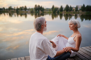Romantic holiday. Senior loving couple sitting together on lake bank.