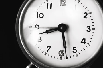 A black-and-white image of the dial of an old clock that shows half past eight in the morning. The clock stands on a dark background. The transience of time. The fading past.