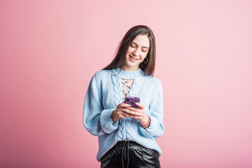 Portrait of a brunette girl on a pink background who uses a smartphone