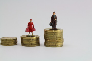 zwei kleine Figuren Frau und Mann stehen auf unterschiedlich hohen Stapeln aus M&uuml;nzen steht f&uuml;r ungleiche Bezahlung und Gleichberechtigung 