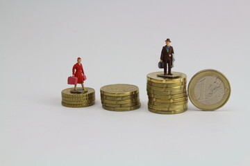 zwei kleine Figuren Frau und Mann stehen auf unterschiedlich hohen Stapeln aus Münzen steht für...