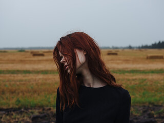 Portrait of a red-haired woman in a black dress in a field in nature cropped view