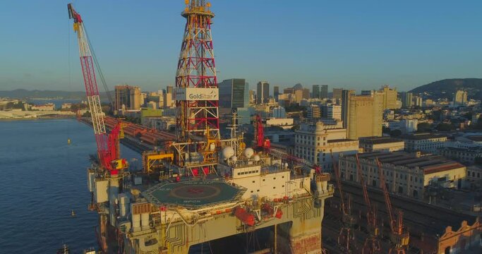 Aerial tracking past industrial oil rig platform to port dockyard district warehouses in Rio de Janeiro Brazil