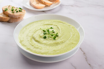 Classic french chilled cream soup vichyssoise - warm or cold potato leek soup topped with microgreens in white bowl on marble table background and bread. Healthy food concept, selective focus