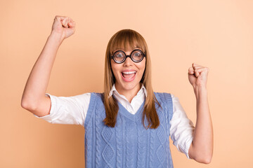 Photo portrait of girl in spectacles wearing blue vest gesturing like winner isolated on pastel beige color background
