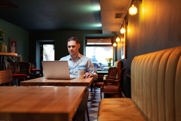 Freelance concept. Handsome young man working on laptop computer while sitting at cafe.