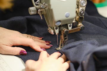Female hands stitching white fabric on professional manufacturing machine at workplace. Close up view of sewing process. Light blurred background