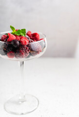 frozen blueberries, raspberries and blackberries on a light textured background. in a tall transparent cocktail glass. copyspace