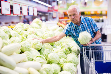 Fototapeta premium Elderly retired man buying cabbages in grocery department of the supermarket