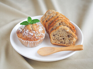 Banana cake sliced in white ceramic dish with wooden spoon placed on brown cloth, Decorate on top with Peppermint leaf and icing sugar, Activity making sweet dessert or, Cupcake at home in holiday.
