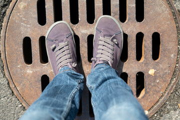 A woman feet stand on the rusty metal cover of the sewage, on a summer day. 