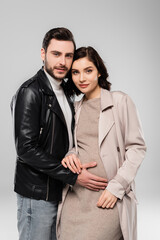 Stylish man standing near pregnant wife isolated on grey